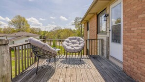 A wooden deck with two chairs and a table, a brick wall, and a window. - Furnished 2BR Retreat with Private Garage (Kansas City)