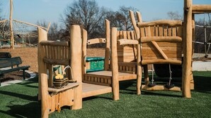 A wooden play structure with a slide and climbing elements, a bench, and a green storage box. - Furnished 2BR Retreat with Private Garage (Kansas City)