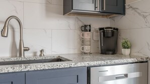 A kitchen with a stainless steel sink, a coffee maker, and a potted plant. - Furnished 2BR Retreat with Private Garage (Kansas City)