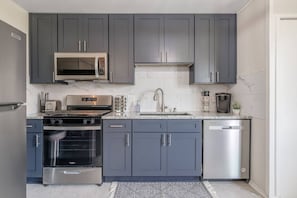 Una cocina moderna con gabinetes grises, electrodomésticos de acero inoxidable, microondas, estufa, horno y lavavajillas.