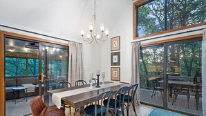 A dining area with a wooden table, chairs, and a chandelier. There are framed pictures on the wall and a sofa with a view of the outdoors. - Bryce Resort | Hot Tub | Game Room | Sleeps 12 (Basye)