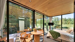 A modern interior with large glass windows, a round wooden table, and a comfortable seating area.