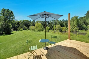 A wooden deck with a table and chairs, a large umbrella, and a view of a grassy area and trees. - ÖÖD Texas Mirror House (Houston) (Coldspring)