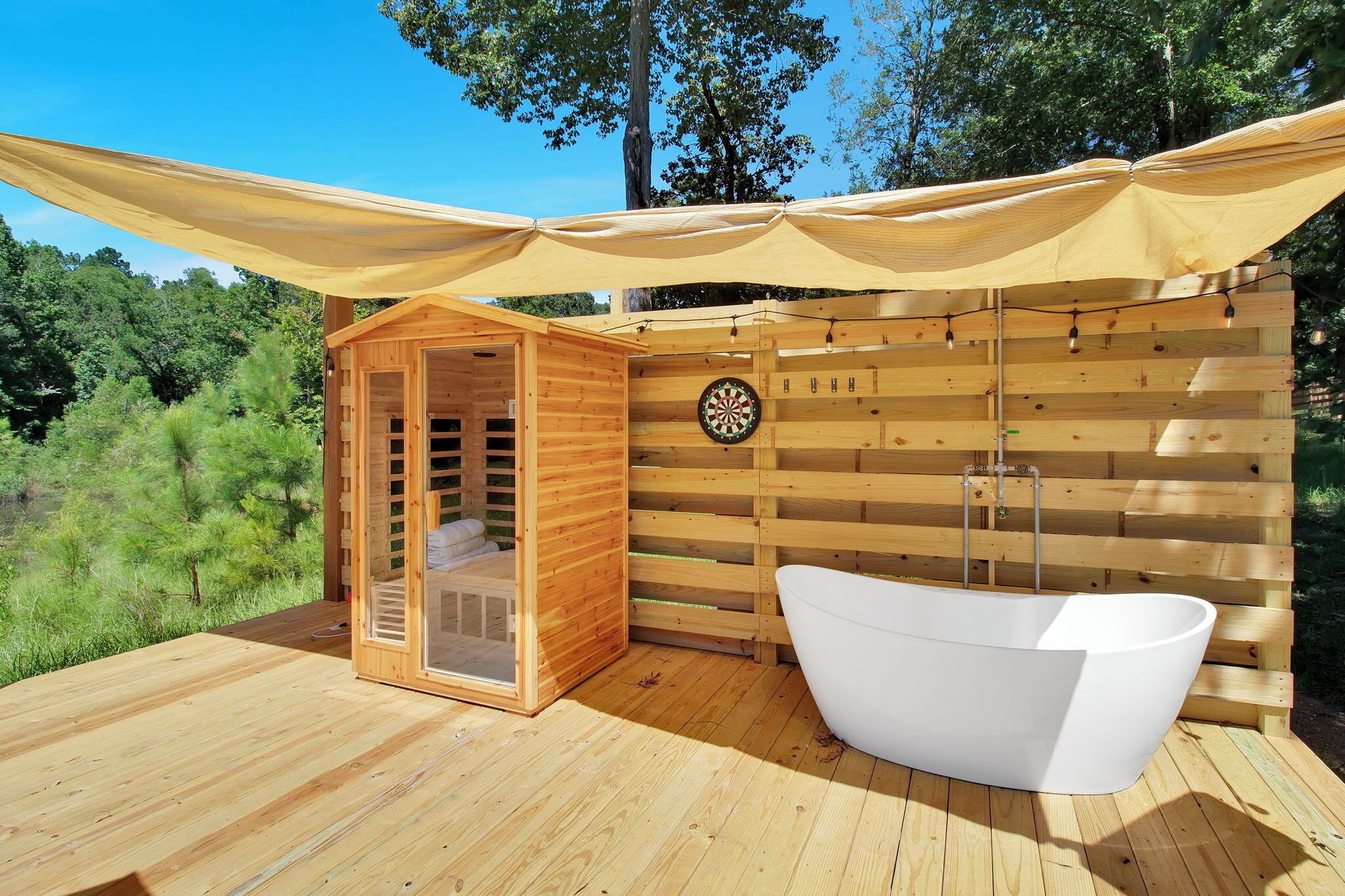 Una sauna de madera con puerta de vidrio, una bañera blanca y un dardo en la pared.