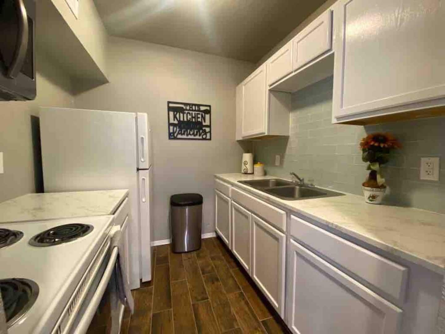 A kitchen with white cabinets, a stainless steel sink, and a trash can.