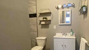 Ein Badezimmer mit Toilette, Waschbecken mit Spiegel und Ablagefläche mit Pflanze.
