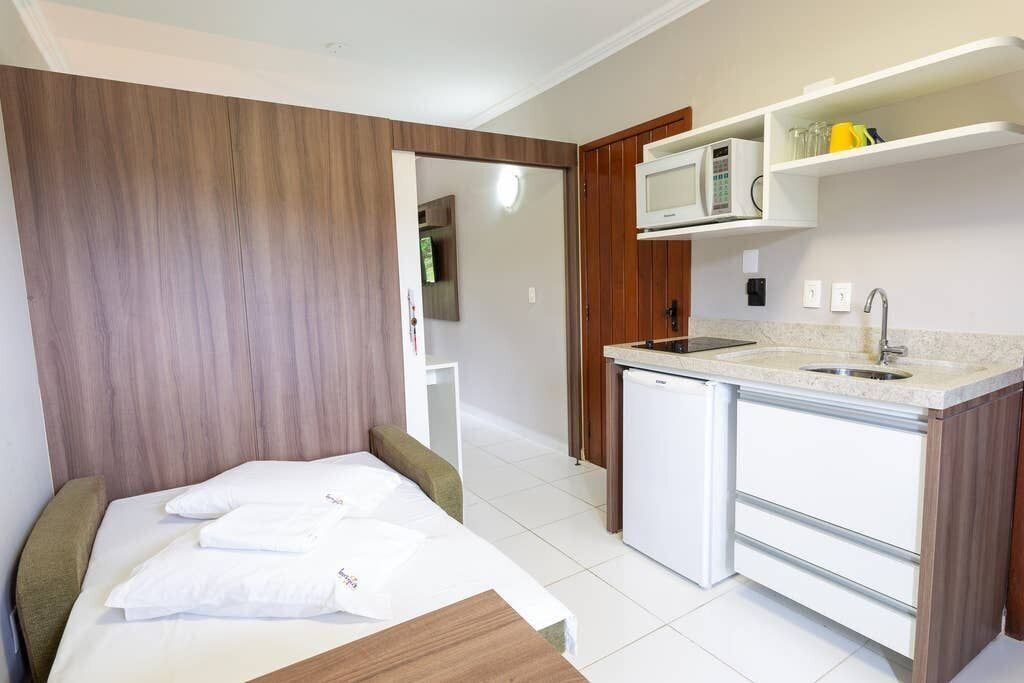 A compact hotel room with a bed, a small kitchenette, and a bathroom visible through an open door.
