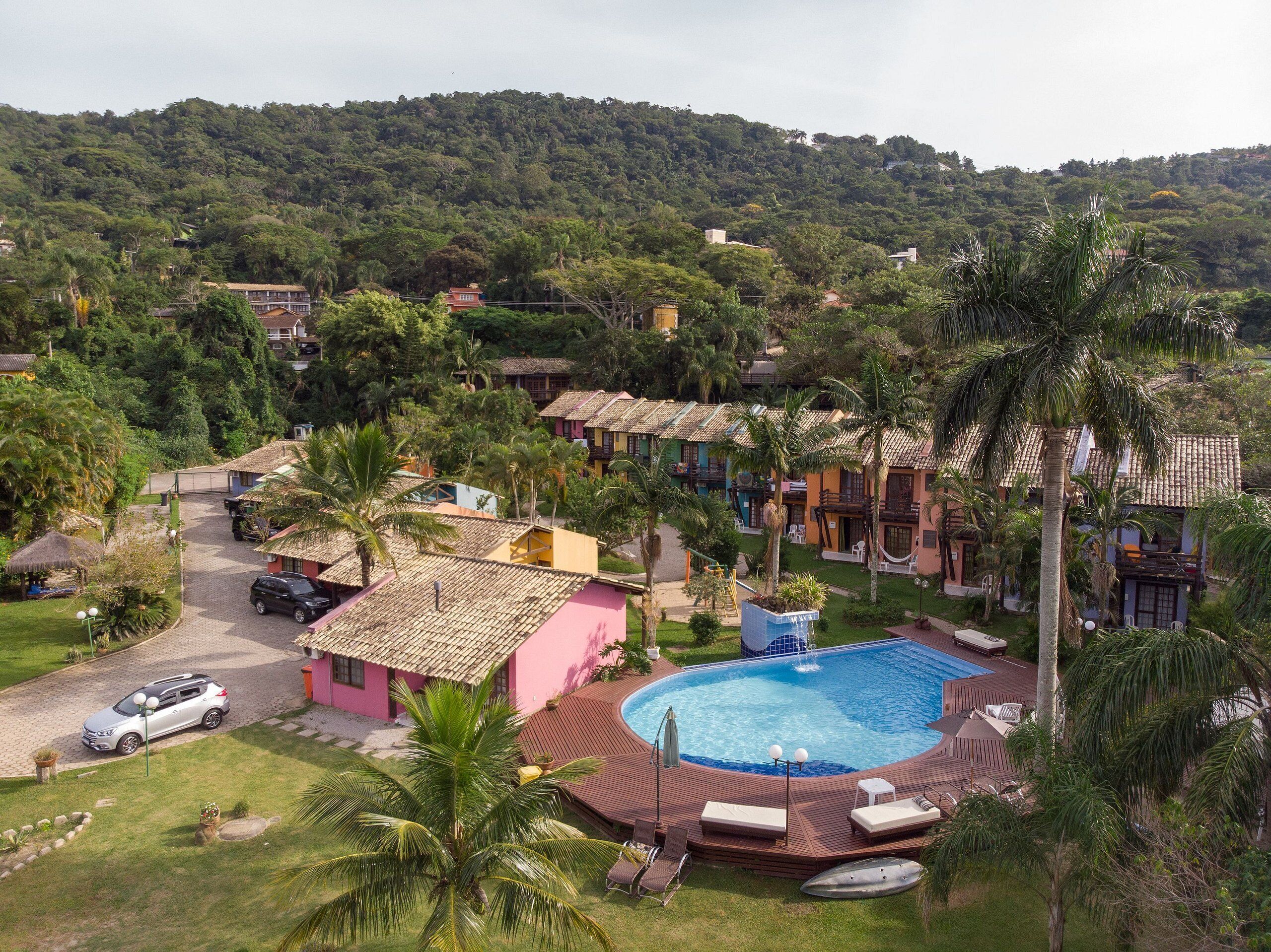 A resort with a swimming pool, palm trees, and houses with red roofs.