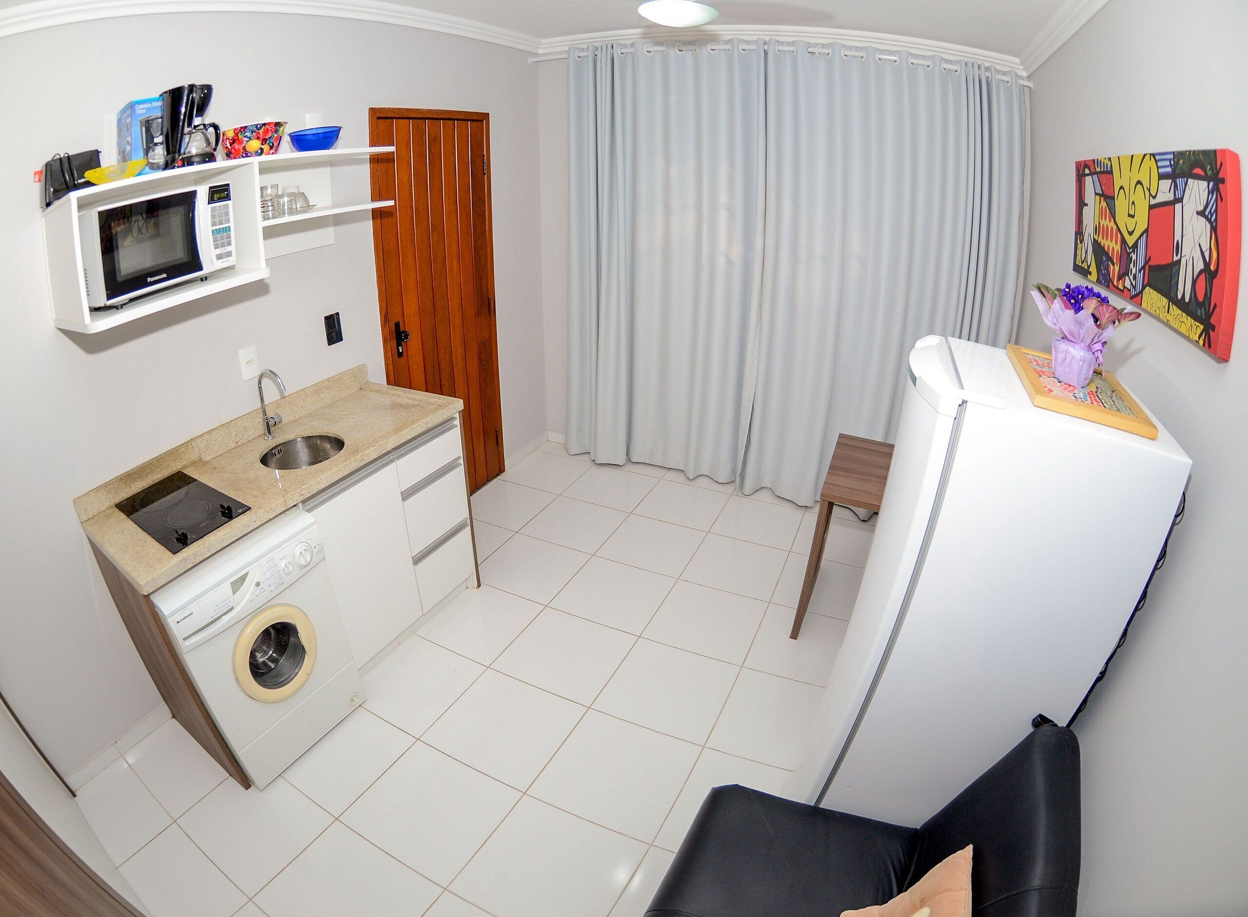 A compact kitchen with a microwave, sink, and washing machine. There's a dining area with a chair and a table.
