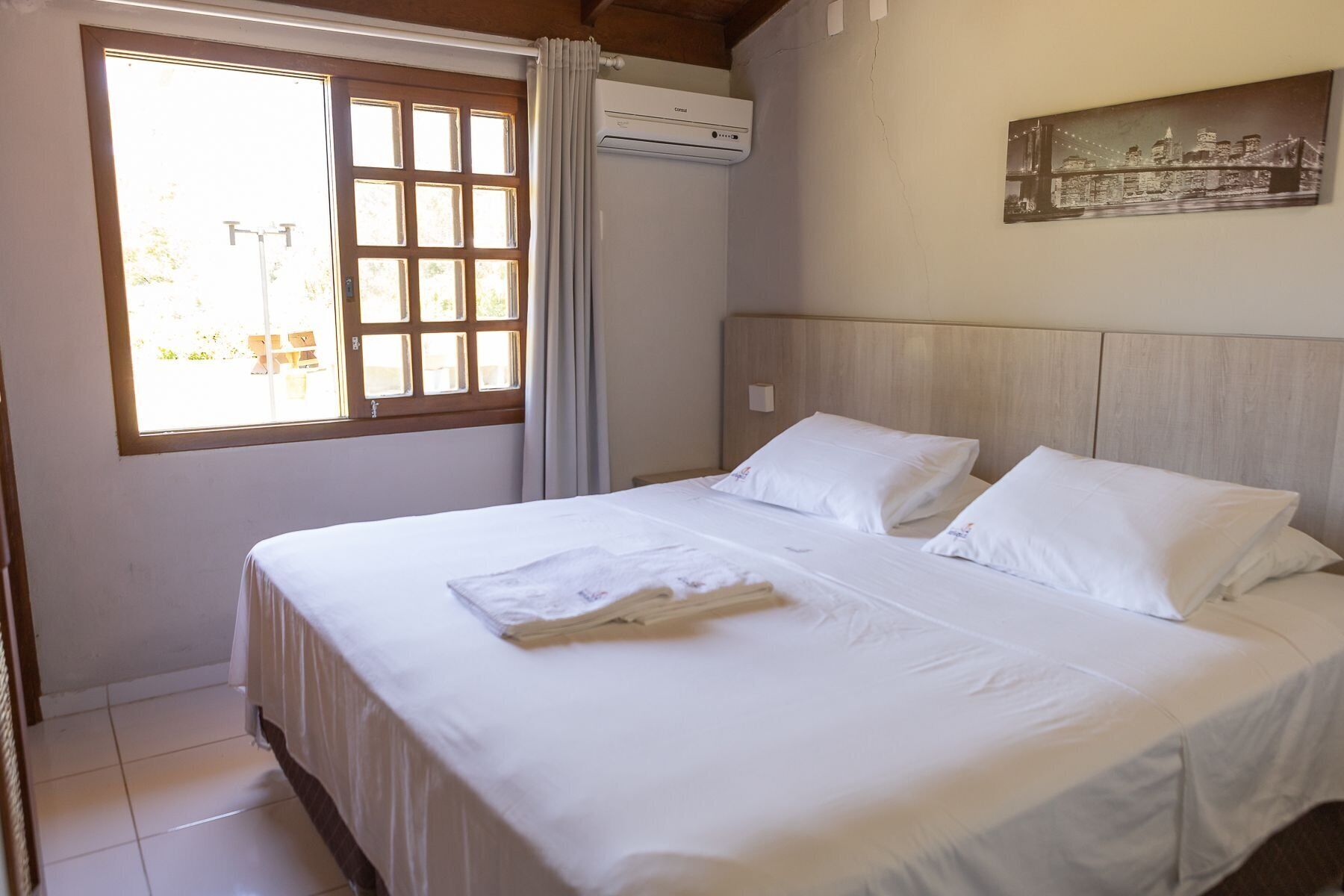 Habitación de hotel con una cama grande, una ventana con cortinas, un aire acondicionado y un cuadro en la pared.
