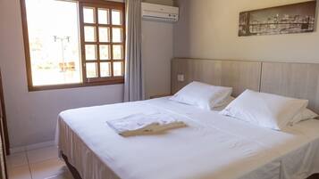 Habitación de hotel con una cama grande, una ventana con cortinas, un aire acondicionado y un cuadro en la pared.