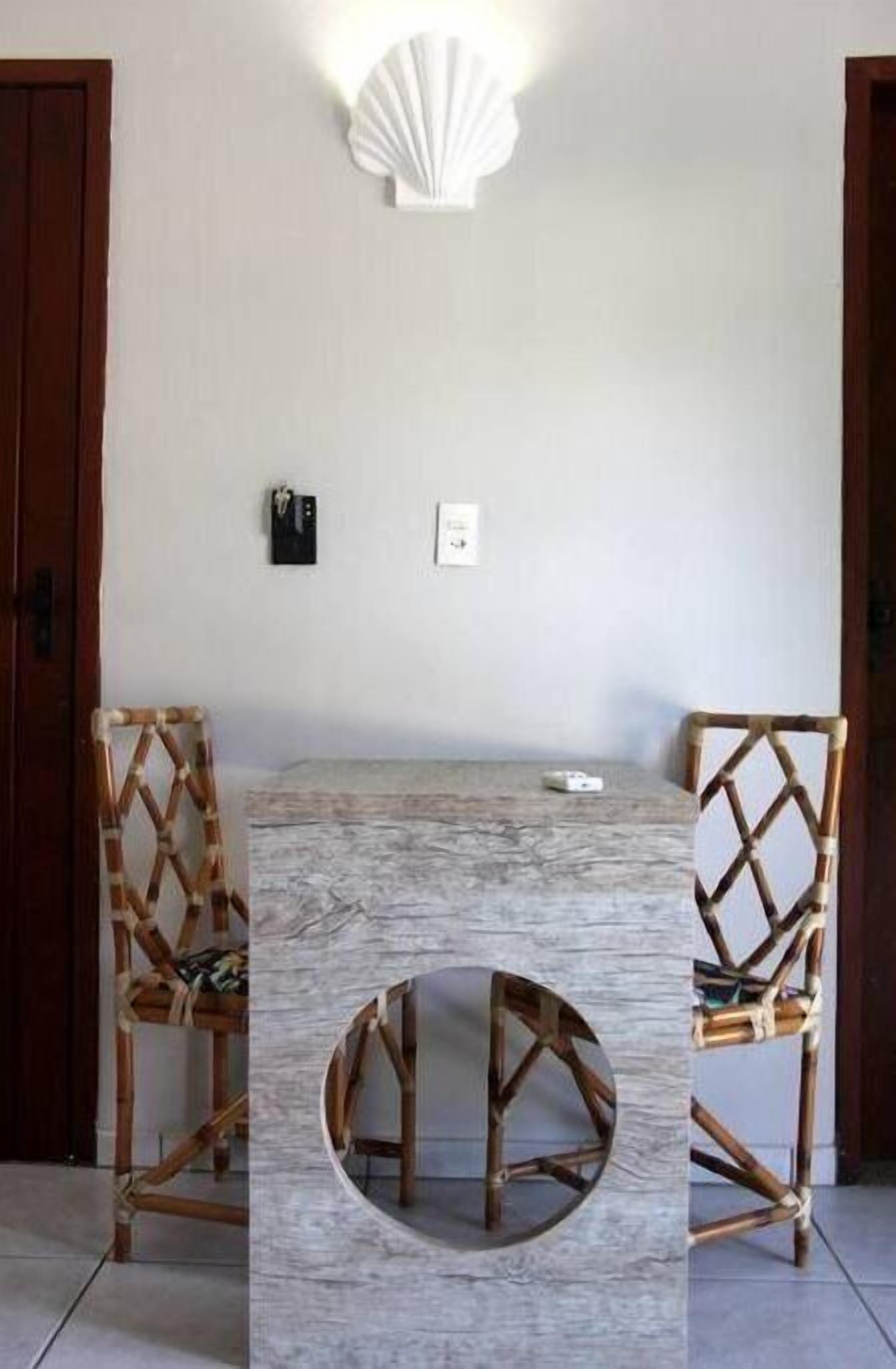 A dining area with a marble table and woven chairs, a wall-mounted light fixture, and a door.