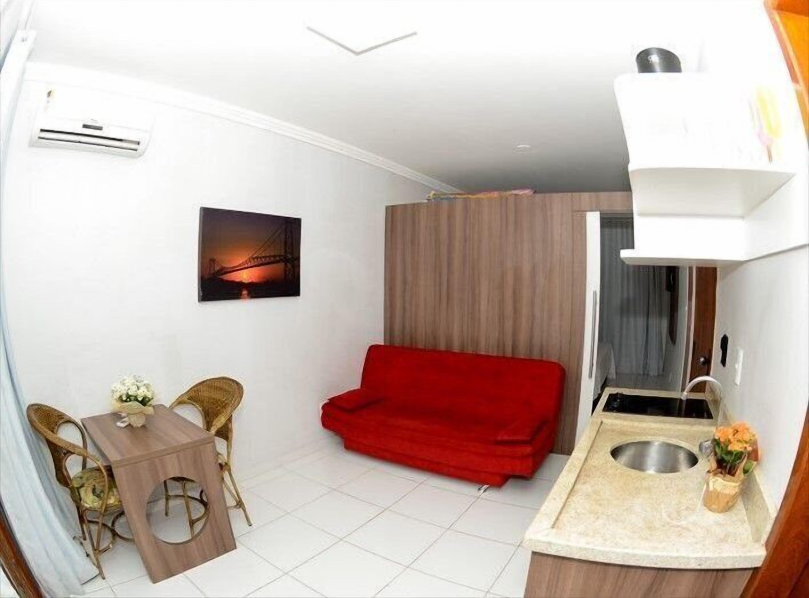 Un espacio habitable compacto con kitchenette, una zona de comedor con mesa y sillas, un sofá rojo y un cuadro de un puente.