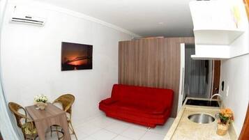 Un espacio habitable compacto con kitchenette, una zona de comedor con mesa y sillas, un sofá rojo y un cuadro de un puente.
