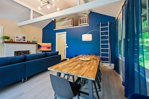Un salon moderne avec une table à manger en bois, un canapé bleu et un escalier menant à un niveau supérieur.