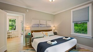 Ein ordentlich eingerichtetes Schlafzimmer mit Bett, Nachttischen, einem Schreibtisch und einem Fenster mit Jalousien.