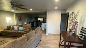 A spacious living room with a large sectional sofa, a dining table with chairs, and a kitchen area in the background.