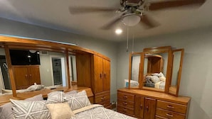 A bedroom with a large bed, wooden wardrobe, and a ceiling fan.