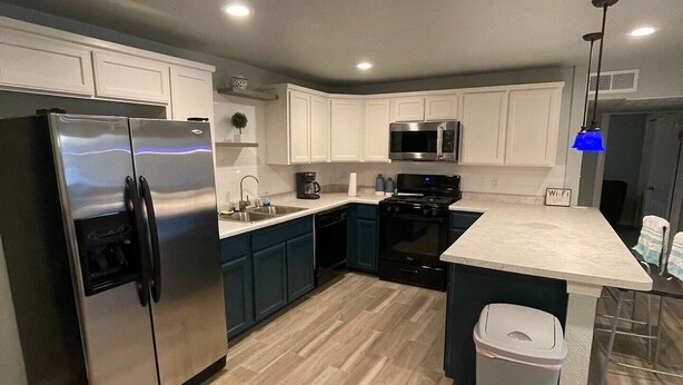 A modern kitchen with white cabinets, stainless steel appliances, and a herringbone wood floor.
