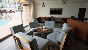 Ett modernt vardagsrum med utsikt över poolen, inrett med ett runt soffbord, soffor och en tv.