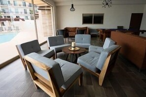 A modern living room with a pool view, featuring a round coffee table, sofas, and a TV. - Luxury Apartment with Pool, Gym, Barbecue in San Jose del Cabo (San José del Cabo)