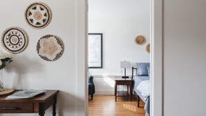 Una stanza con pavimento in legno, un letto con coperta blu, un comodino con lampada e una mappa incorniciata appesa al muro.