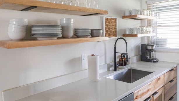 Una cucina con ripiani in legno che contengono piatti e bicchieri, una macchina del caffè e un lavandino.