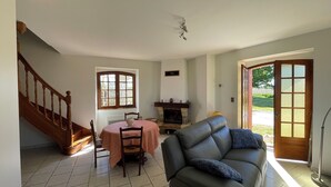 A living room with a fireplace, a sofa, a dining table with chairs, and a staircase. - Maison de Campagne Avec vue sur la Chaîne des Pyrénées (VIC-EN-BIGORRE)