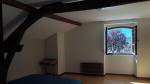 An attic bedroom with a sloped ceiling, a small table, a radiator, and a window with a view of trees. - Maison de Campagne Avec vue sur la Chaîne des Pyrénées (VIC-EN-BIGORRE)