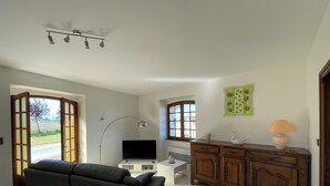 A living room with a sofa, a TV, a cabinet, and a window with a view of the outdoors. - Maison de Campagne Avec vue sur la Chaîne des Pyrénées (VIC-EN-BIGORRE)