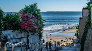 Un sendero costero que lleva a una playa, con una escalera y una cerca adornada con plantas en flor.