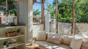 Un rincón acogedor con un banco acolchado, una mesa redonda pequeña y estantes con objetos decorativos.