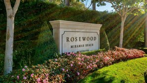 Letrero de Rosewood Miramar Beach con un jardín cuidado y árboles al fondo.