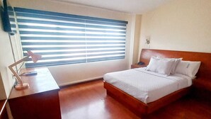 Un dormitorio con cama de madera, un escritorio con lámpara y una ventana con persianas.