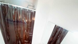 Un baño con cortina de ducha, dos inodoros, un lavamanos y un espejo.