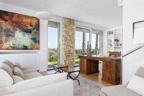 A modern living room with a large abstract painting, a stone pillar, a wooden desk, and a staircase.