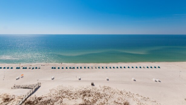 A beach with rows of tents and a wooden walkway leading to the water.
