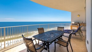 A balcony with a table and chairs, overlooking the ocean.