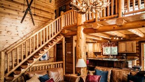 L’intérieur d’une cabane en rondins, avec un escalier en bois, des canapés en cuir et un coin cuisine.