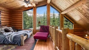 Une chambre confortable dans un chalet, avec un lit, un fauteuil rouge et une grande fenêtre donnant sur une vue imprenable sur les montagnes.