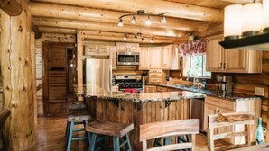 L’intérieur d’un chalet rustique, avec des murs en bois, un îlot central doté de tabourets et un espace cuisine équipé d’appareils électroménagers.