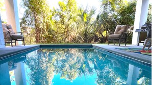 Una piscina amb aigua cristal·lina que reflecteix els arbres del voltant i una barbacoa al fons.