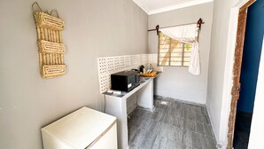 A compact kitchen with a refrigerator, a microwave, and a sink. There is a window with a curtain and a wall-mounted basket. - Mama's House (Zanzibar Town)