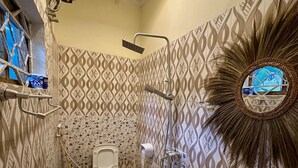 A bathroom with patterned walls, a toilet, a sink, a shower, and a ceiling-mounted fan. - Mama's House (Zanzibar Town)