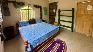 A bedroom with a bed, a ceiling fan, a window with a view, a door, and a green shelf. - Mama's House (Zanzibar Town)