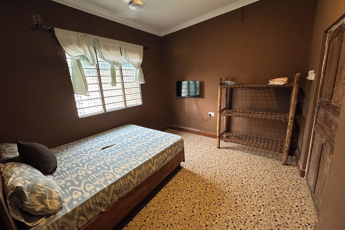 A bedroom with a bed, a window with curtains, a wall-mounted TV, and a bunk bed.