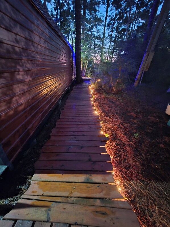Un sentier en bois traverse une zone boisée, avec un mur en bois d’un côté.