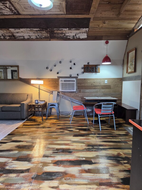 A room with a wooden ceiling, a wall clock, a red pendant light, and a television.
