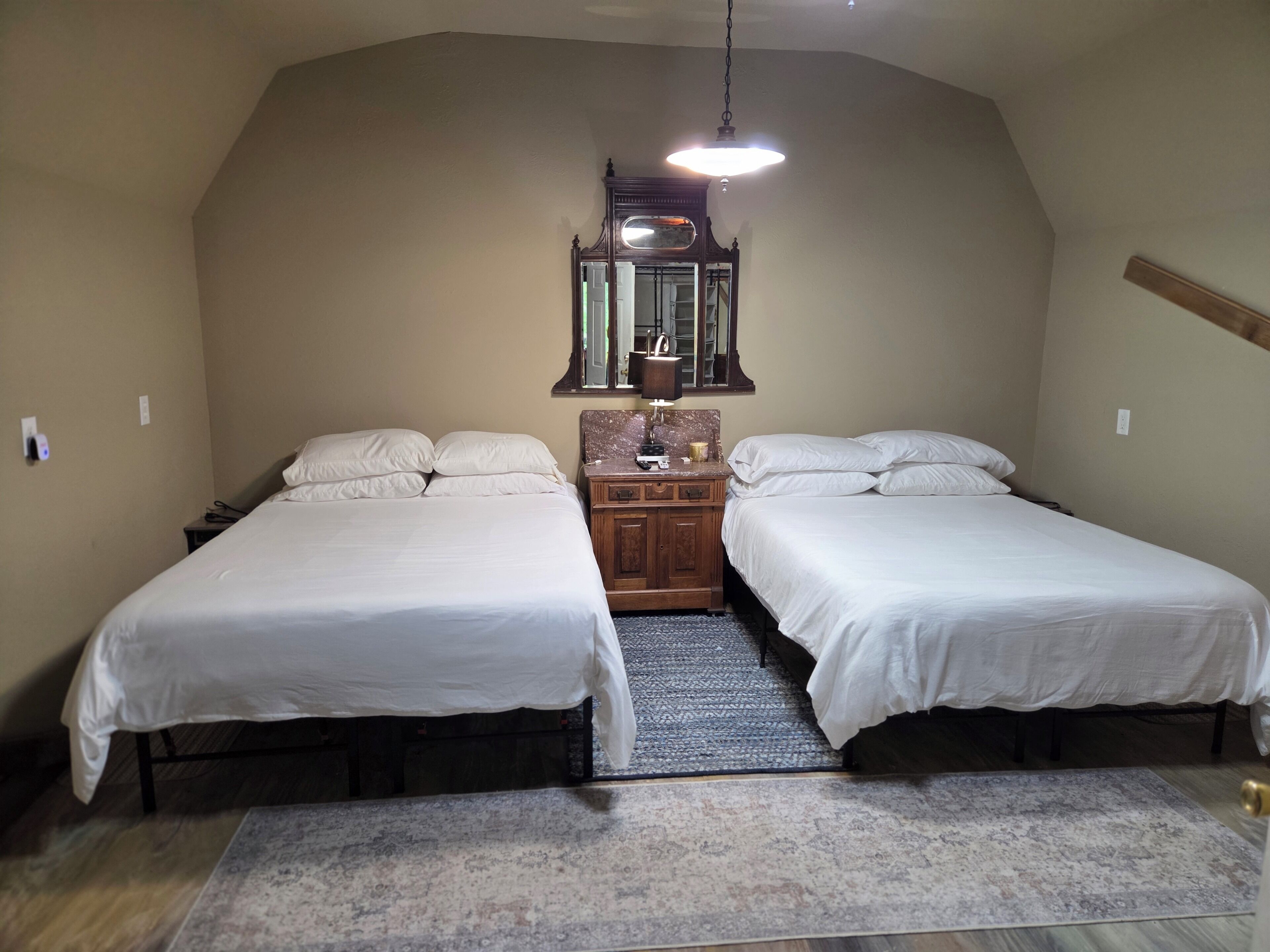 Una camera da letto con due letti, una cassettiera in legno, uno specchio e una lampada a sospensione.