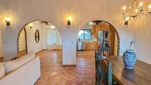 A spacious interior with a stone-tiled floor, wooden ceiling beams, and a dining area with a wooden table and chairs.